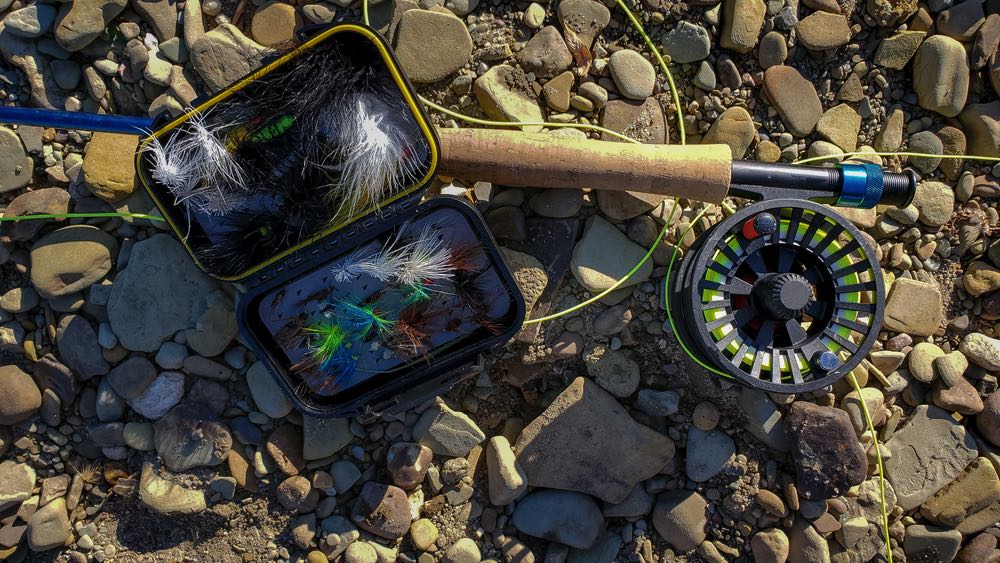 https://intoflyfishing.com/wp-content/uploads/2020/07/fly-rod-and-reel-with-flies-on-river-rocks.jpg