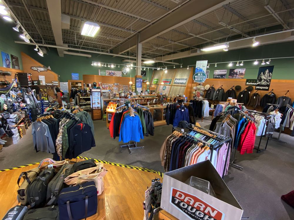 Inside a fly shop in Virginia, with racks of jackets and gear and rod brand banners along the walls