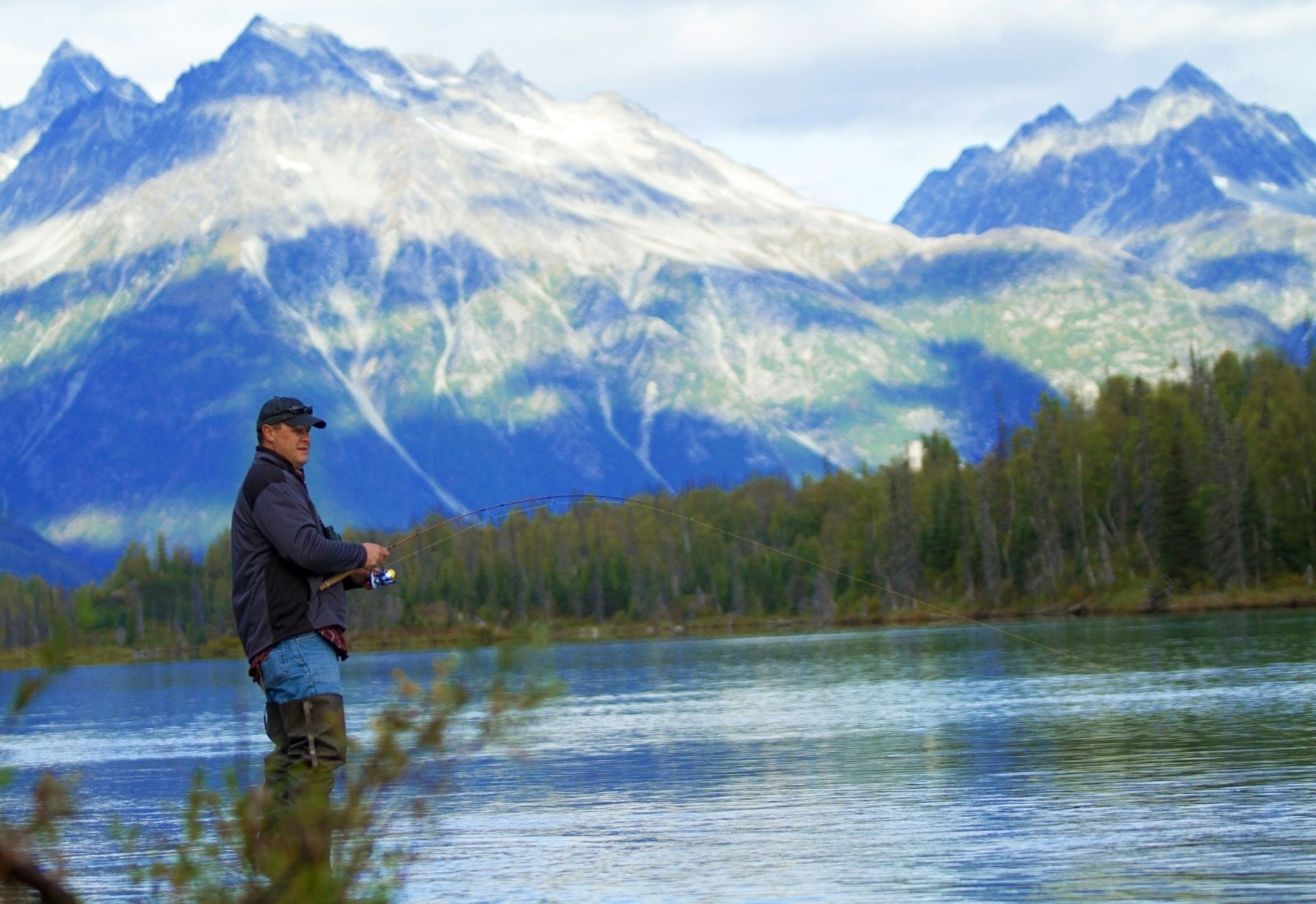 Angler fishing with mountains behind the river
