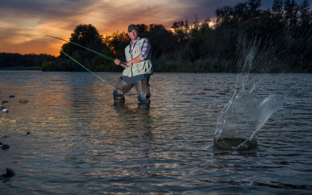 An angler lands a big one on the river at sunset.