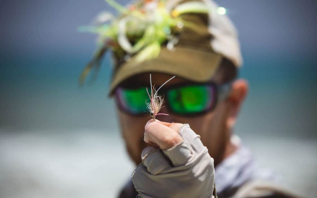 An angler is holding a saltwater fly in a blurry background.
