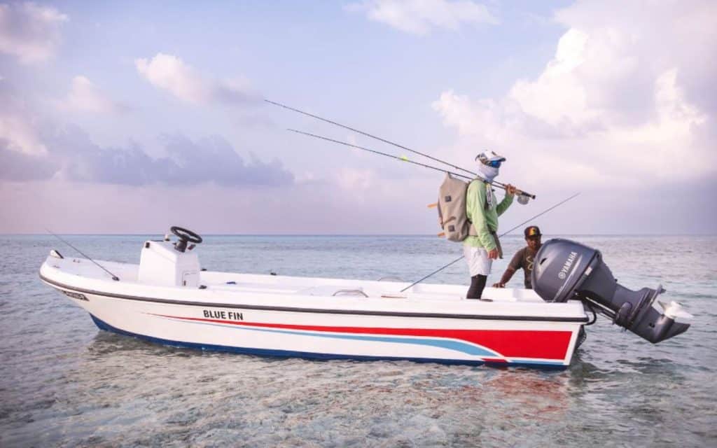 An angler standing on a fishing boat while carrying some saltwater fly rods with a backpack.