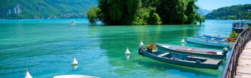 A nice Photo Lake Annecy on a calm day with boats in the foreground and a tree covered island.