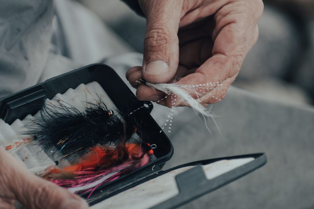 Hands selecting a fly pattern from a fly box, showing the type of hook the Palomar knot connects to tippet