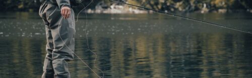 Fly angler in waders, standing in still water with fly line extended, preparing to cast