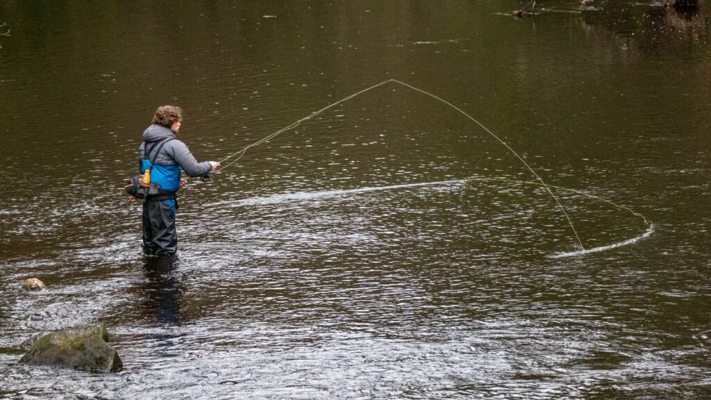 Angler casting a fly rod in a river, showing how current and water level affect where fish hold