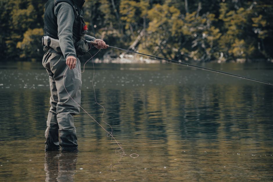 Fly angler standing in calm water holding a rod, managing fly line for a natural drift