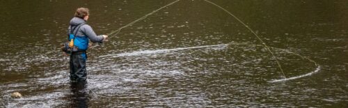 Fly fisher wading in a river, preparing to cast a fly rod