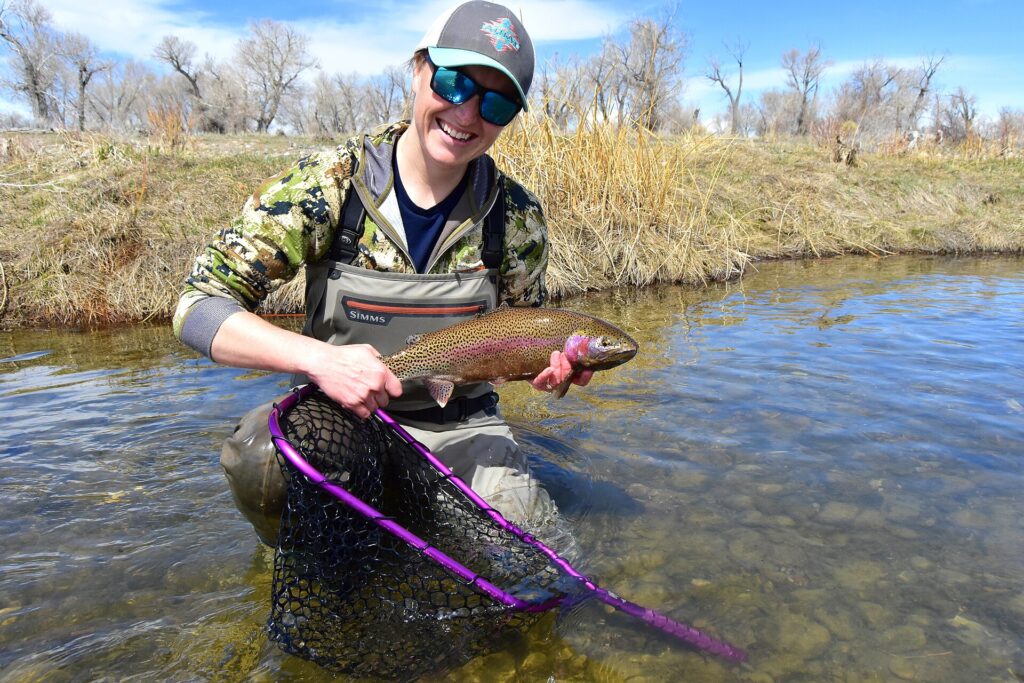 Fly angler holding a trout beside a shallow stream