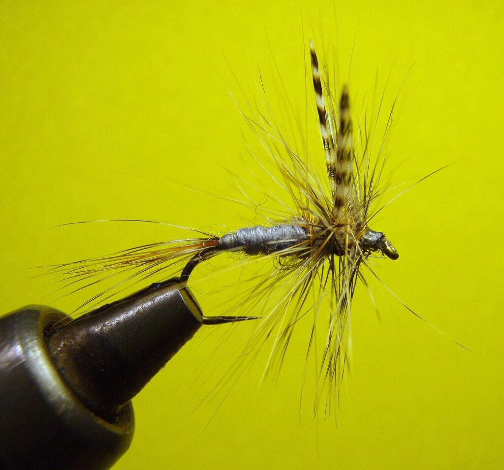 Adams dry fly tied on a hook and held in a vise