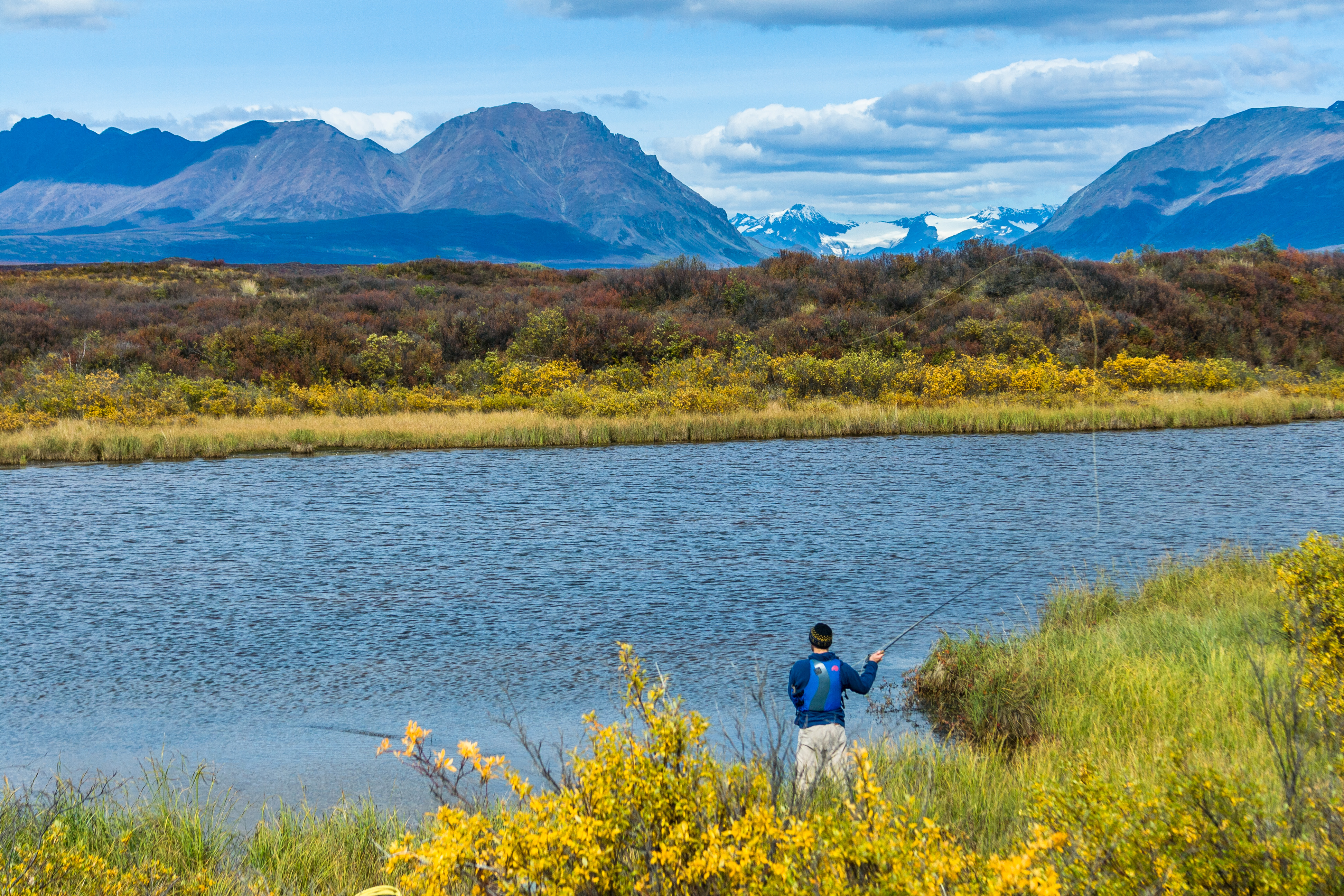An angler fly fishing at Tangle Lakes beneath the Alaska Range
