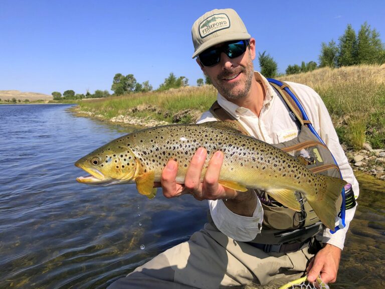 Angler holding a brown trout beside a river